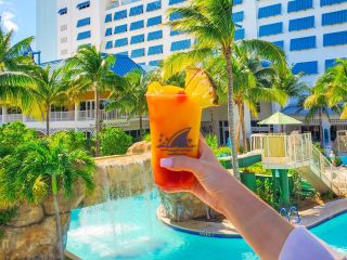 A Hand Holding A Glass Of Orange Juice In Front Of A Hotel